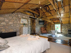 A bedroom with a stone wall, a bed with a white bedspread, a chair, a bathtub, and a television.
