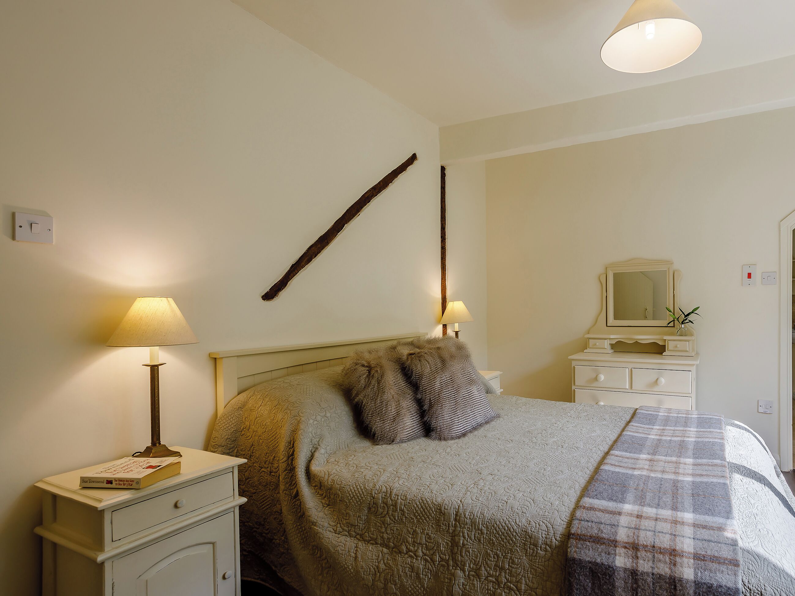 A bedroom with a bed, bedside lamps, a dresser, a mirror, and a wall-mounted light fixture.