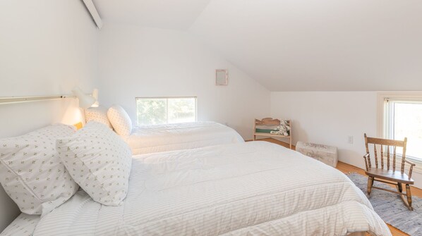 Un dormitorio con dos camas, una ventana, una silla de madera y una mesita de noche.