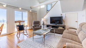 A spacious living room with a large window, a television, a sofa, a rocking chair, and a coffee table.