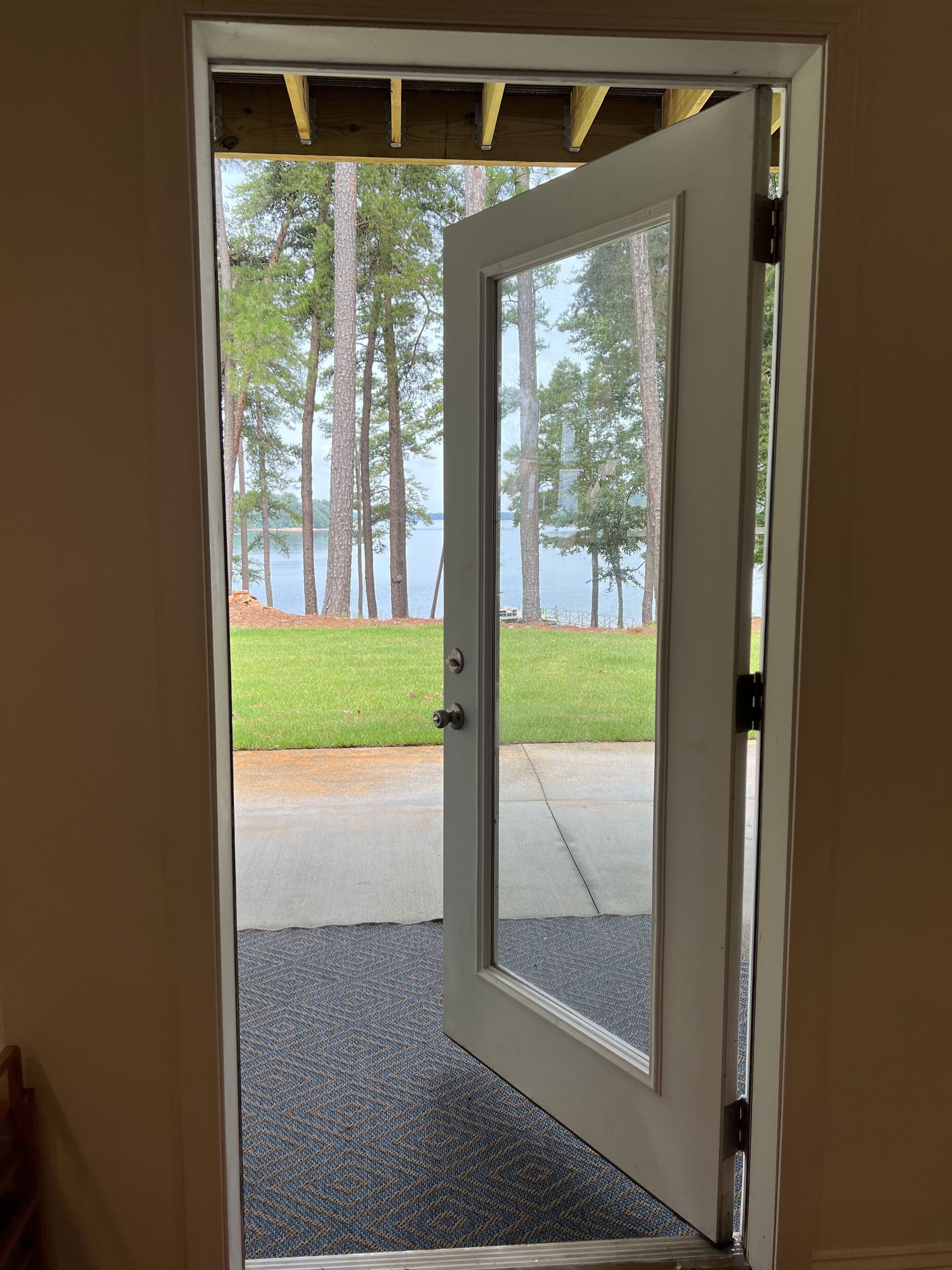 A door leading to a view of a lake with trees and a grassy area.