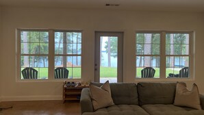 Un salon spacieux avec un grand canapé d’angle, un porte-chaussures en bois et une vue sur un lac, visible à travers de grandes fenêtres.