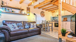 A cozy living room with a leather sofa, a dining table, and a kitchen in the background. - The Hideaway Low Hawsker (Low Hawsker, near Whitby)