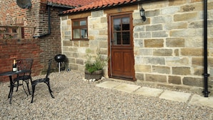 A stone building with a red-tiled roof, a wooden door, and a small garden area with a table and chairs. - The Hideaway Low Hawsker (Low Hawsker, near Whitby)