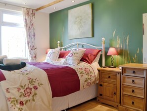 Un dormitorio con cama, mesita de noche, lámpara y una pared con estampado floral.
