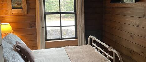 Un dormitorio de cabaña de madera con cama, ventilador de techo, ventana y lámpara.