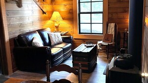 A cozy cabin interior with a wooden ceiling, a sofa, a table with a bowl of fruit, and a wood stove. - Cabin in the Meadow (Sandpoint)