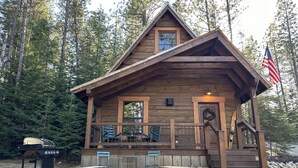 A rustic cabin with a porch, a flag, and outdoor seating. - Cabin in the Meadow (Sandpoint)