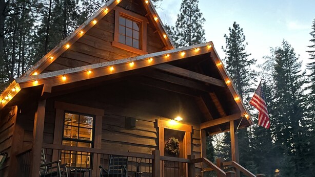 A rustic cabin with a porch, two chairs, a fire pit, and an American flag. - Cabin in the Meadow (Sandpoint)