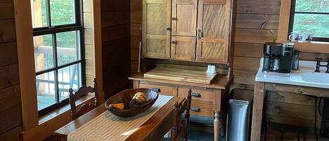 Une cuisine rustique aménagée dans une cabane en bois, avec une table à manger, des placards et une fenêtre donnant sur la verdure.