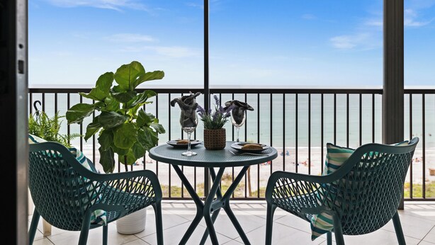 Ein Balkon mit Tisch und Stühlen, einem Blumentopf und Blick auf den Strand.
