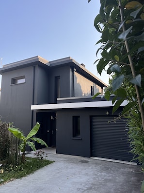 A modern two-story house with a garage, surrounded by greenery.