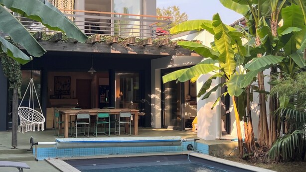 Una casa moderna con piscina, comedor y abundante vegetación.