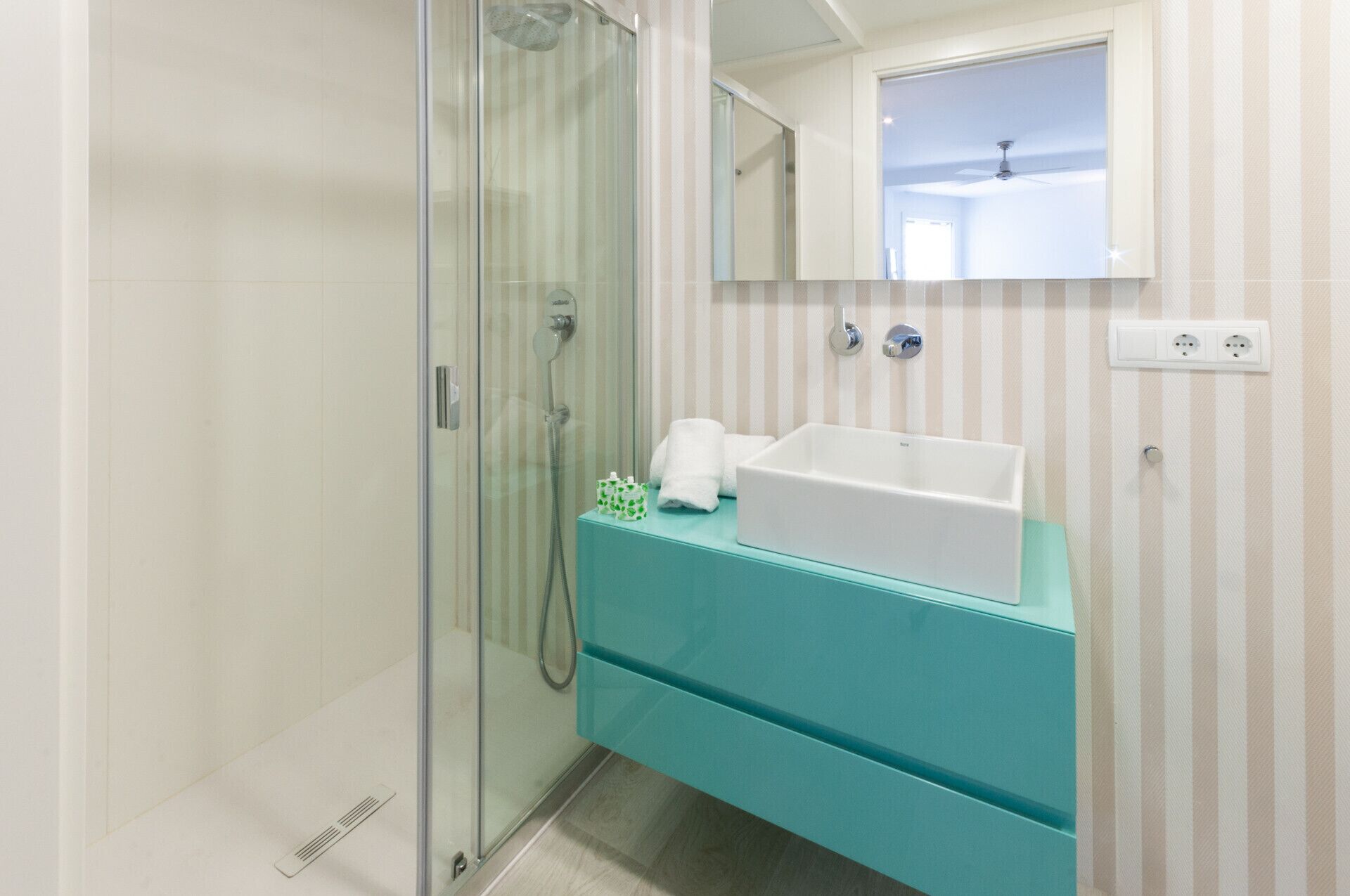A bathroom with a glass shower enclosure, a white sink, and a teal vanity.