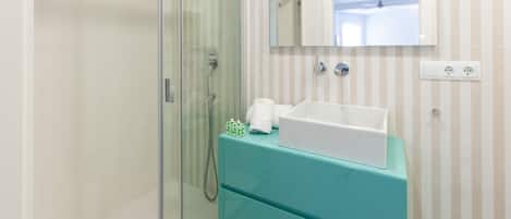 A bathroom with a glass shower enclosure, a white sink, and a teal vanity.
