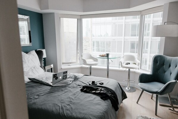 A modern hotel room with a large bed, a laptop, a coffee table, and two chairs.
