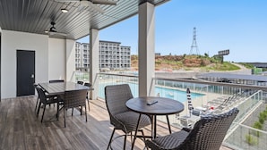Un balcon avec une piscine, des meubles en osier et une vue sur des immeubles et une tour.