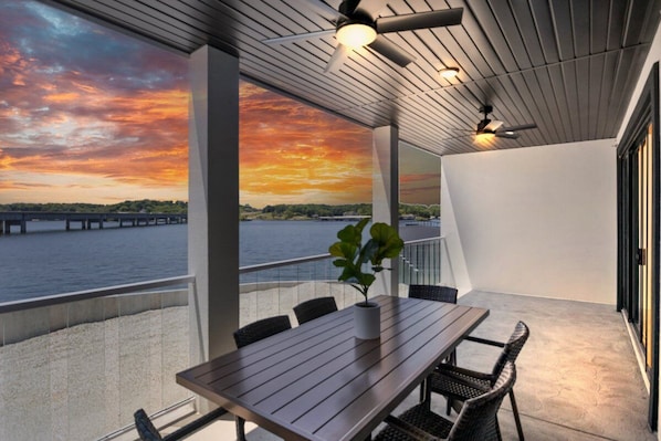 Enjoy breathtaking views of the water and a bridge from this outdoor balcony with a table, chairs, and a potted plant.