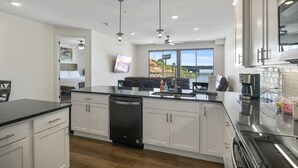 Une cuisine moderne avec des meubles blancs, un lave-vaisselle noir et un grand îlot central doté d’un évier.