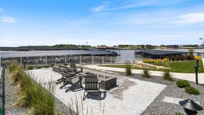 Un espace extérieur aménagé avec des sièges, un foyer et une vue sur un plan d’eau.