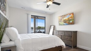 Une chambre à coucher avec un lit, une commode, un ventilateur de plafond, une fenêtre donnant sur un beau paysage et un tableau accroché au mur.