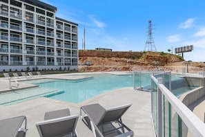 Un hotel con piscina, sillas de descanso y vistas a una colina con una torre de líneas eléctricas.