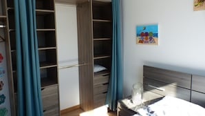 A bedroom with a wooden wardrobe, a bed with a white headboard, and a painting on the wall. - New apartment (La Rochelle)