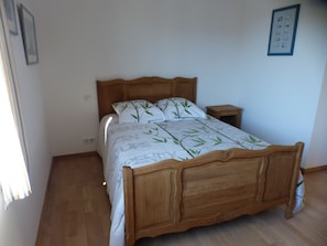 Una cama de madera con colcha estampada con motivos de hojas, una mesita de noche y un cuadro colgado en la pared.