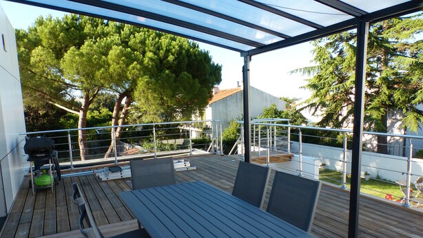 An outdoor patio with a table and chairs, surrounded by a metal railing and trees. - New apartment (La Rochelle)