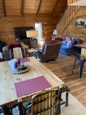 A cozy cabin interior with a wooden dining table, a sofa, and a staircase.