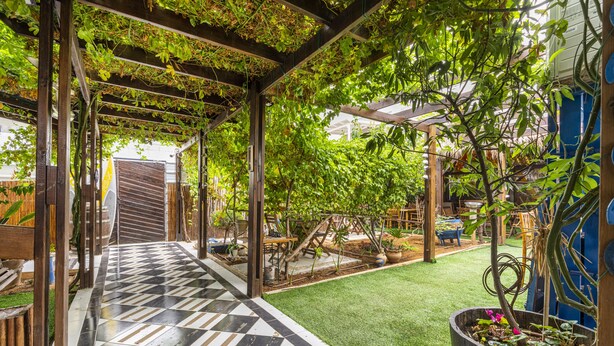 A covered patio area with a checkered floor, wooden pergola, and potted plants. - Ahuzat Shaul Hotel Seaside (Hadera)