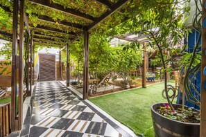 Un'area patio coperta con pavimento a scacchi, una pergola in legno e piante in vaso.