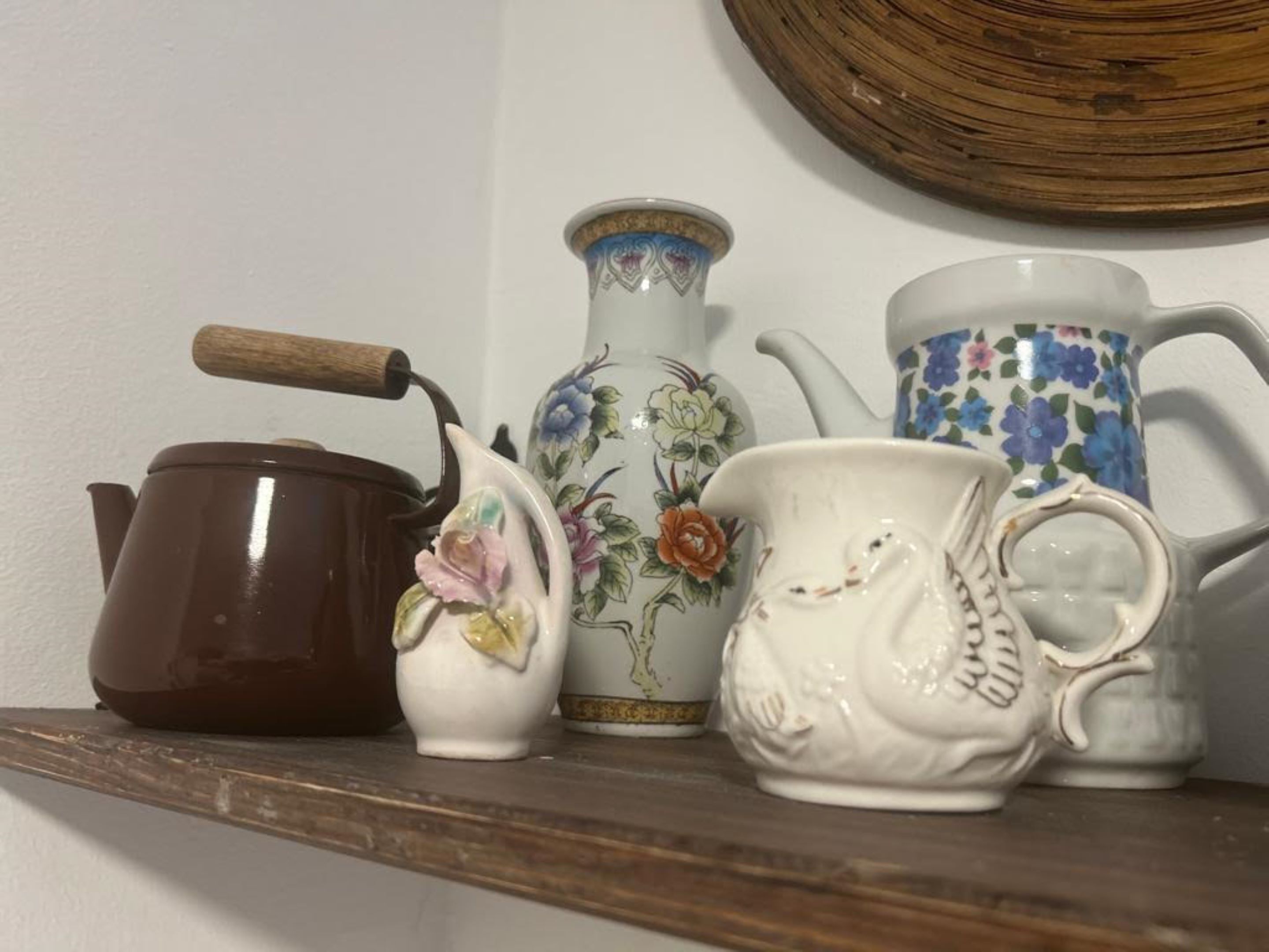 A shelf with a brown teapot, a white pitcher with floral designs, and a white teapot with a handle.
