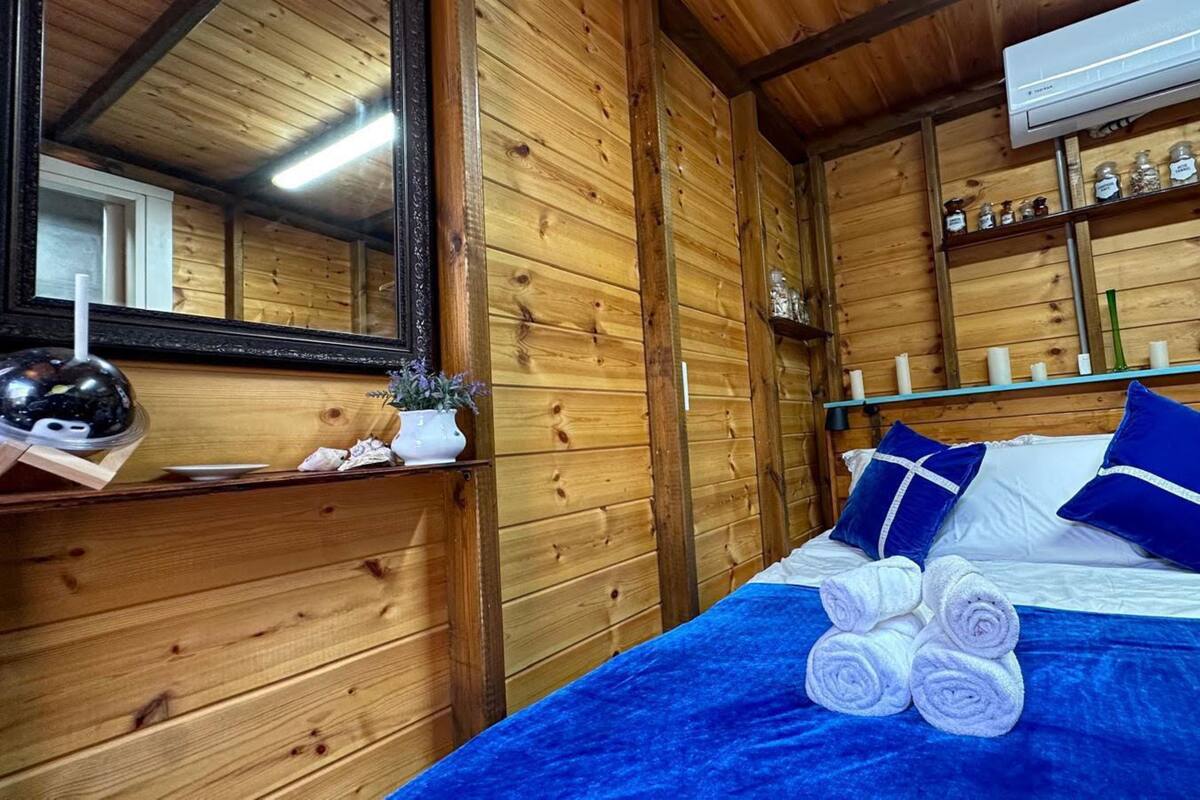 A wooden room with a bed, pillows, a mirror, a shelf with jars, and a wall-mounted air conditioner.