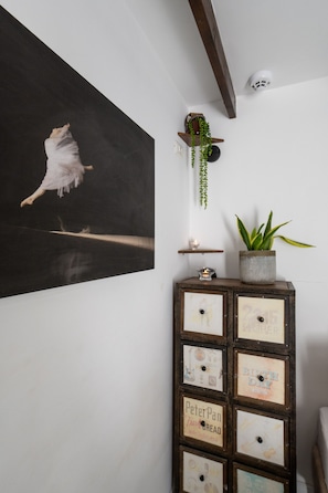 Une pièce décorée d’un tableau en noir et blanc, d’une armoire en bois ornée d’étiquettes anciennes, d’une plante suspendue et d’un luminaire au plafond.