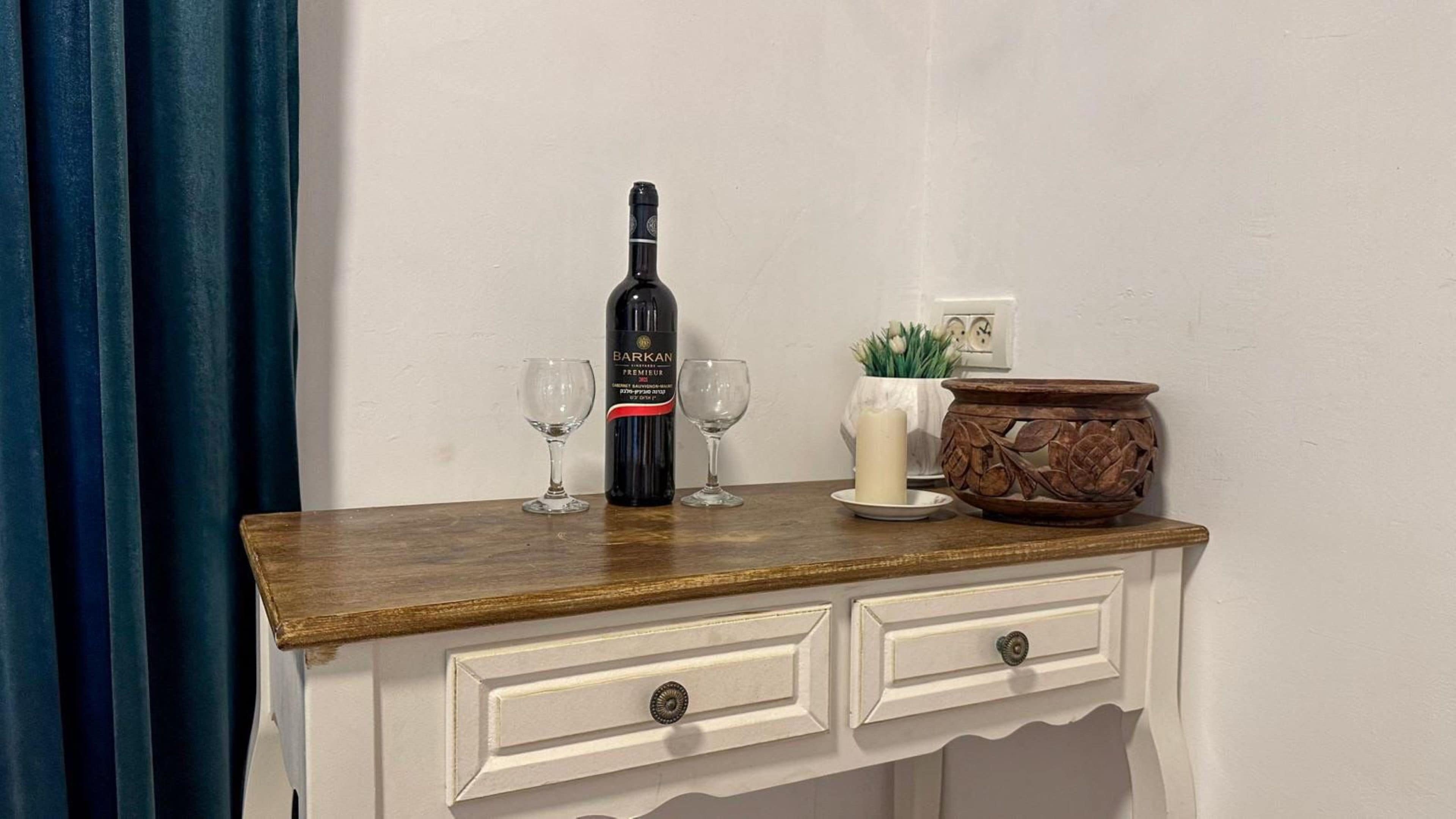 A wooden table with a bottle of wine, two wine glasses, a candle, and a decorative pot.