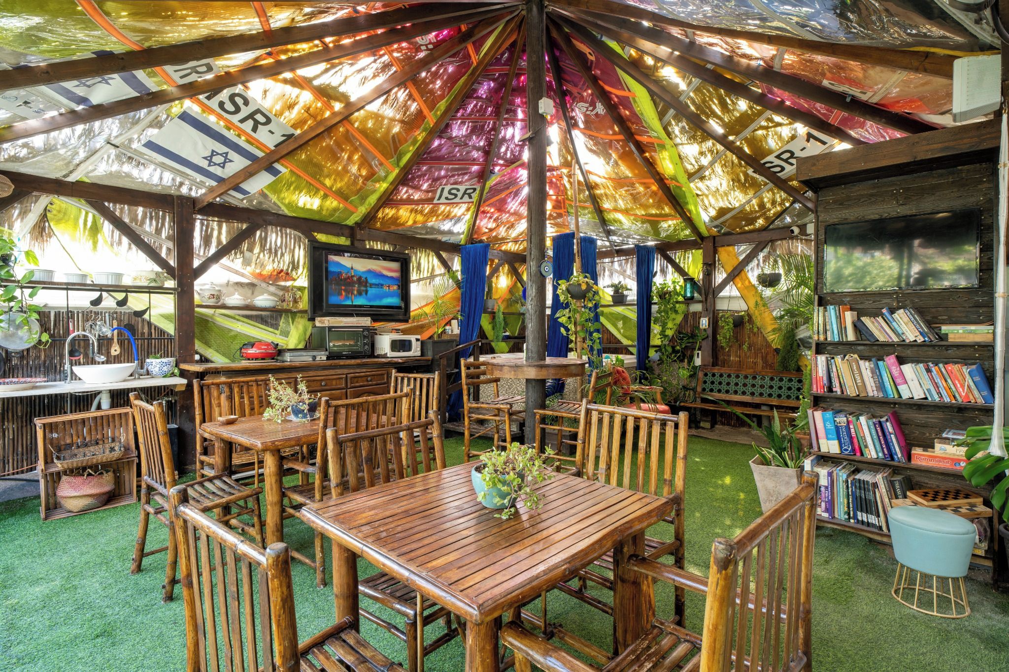 A covered outdoor area with tables and chairs, a television, and bookshelves.