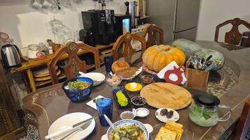 Una mesa de comedor dispuesta con diferentes platos, una máquina de café y un centro de mesa con calabazas.