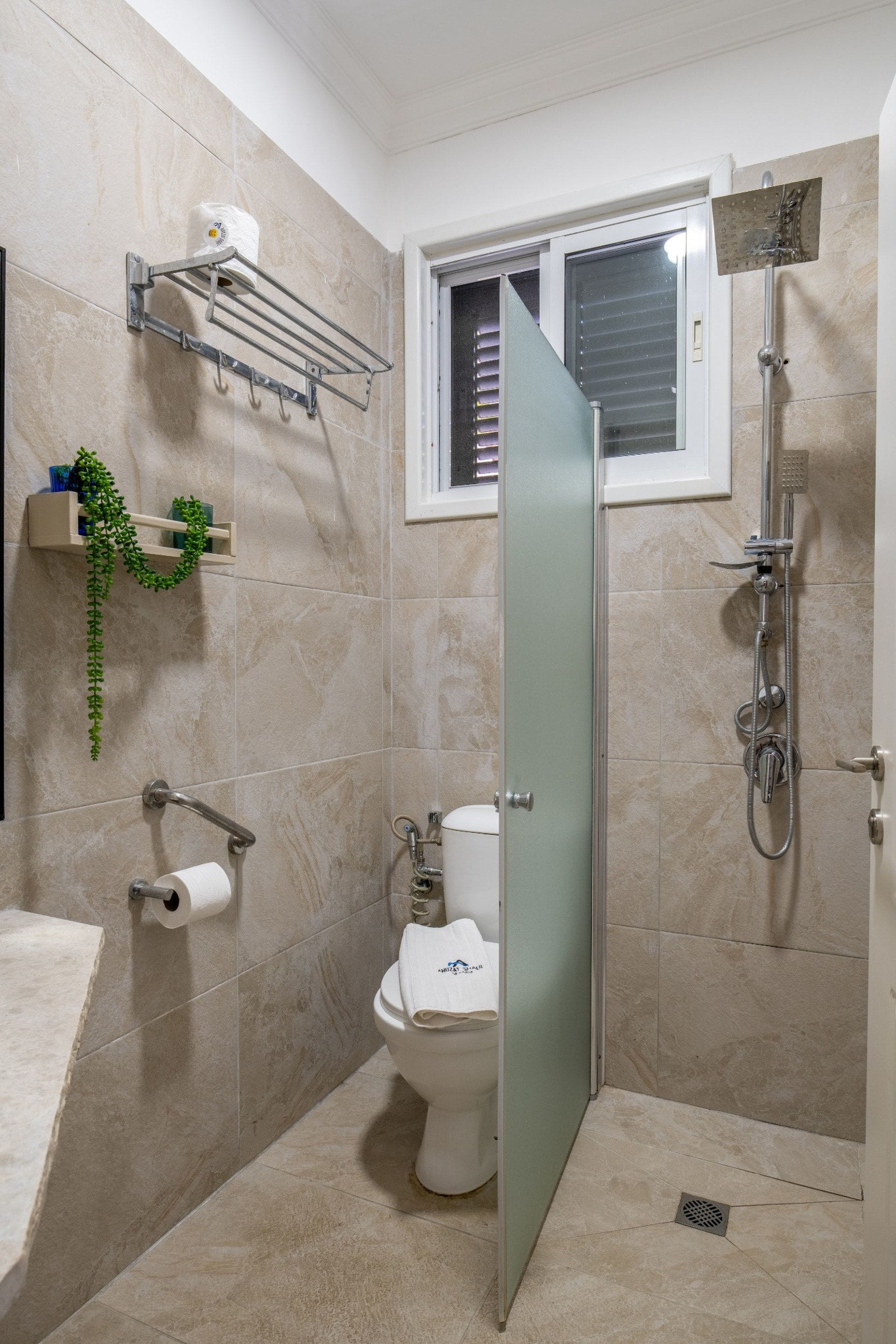 Un baño con inodoro, ducha, toallero y dispensador de papel higiénico.