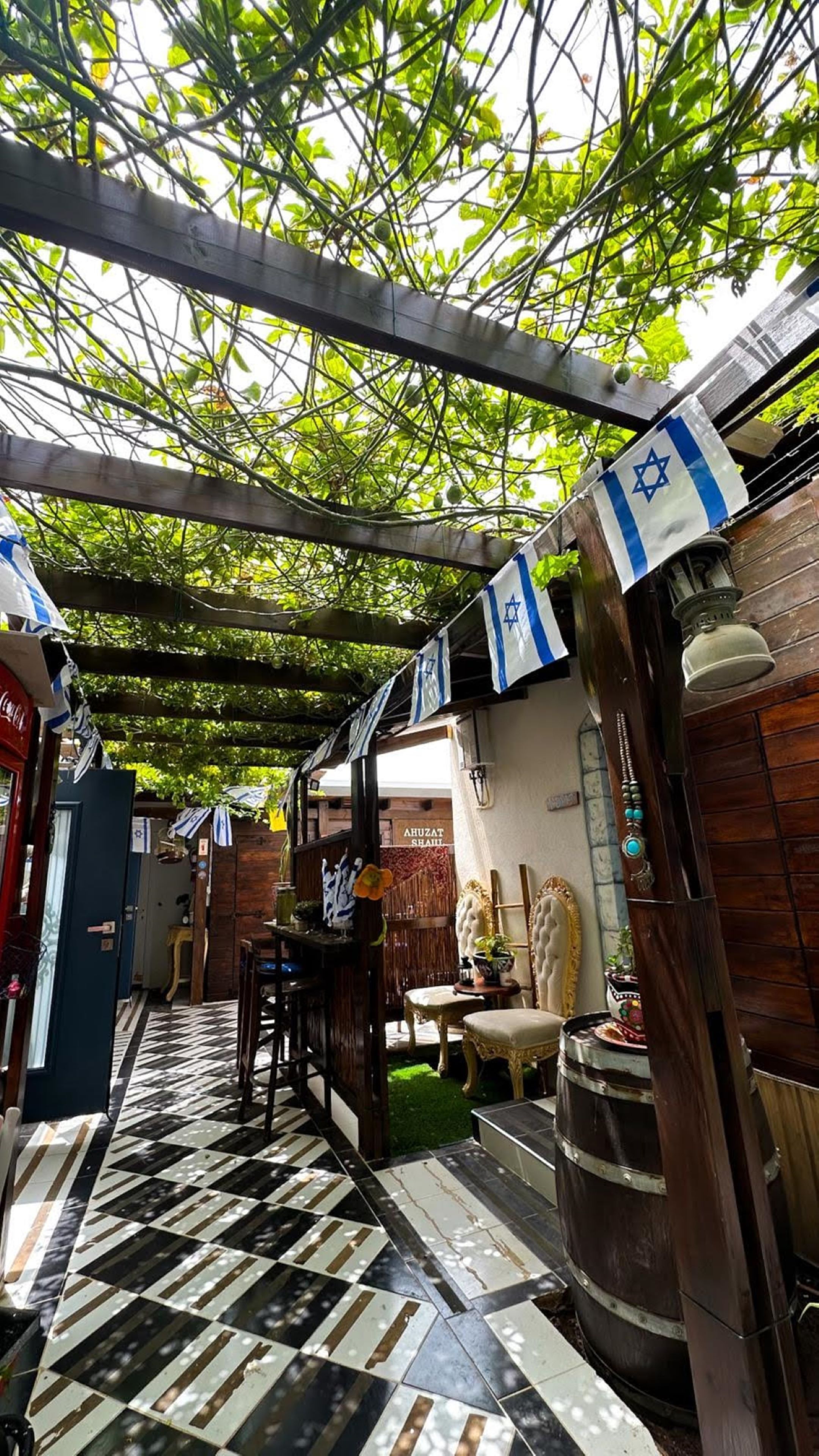 A narrow corridor with a checkered floor, wooden beams overhead, and Israeli flags.