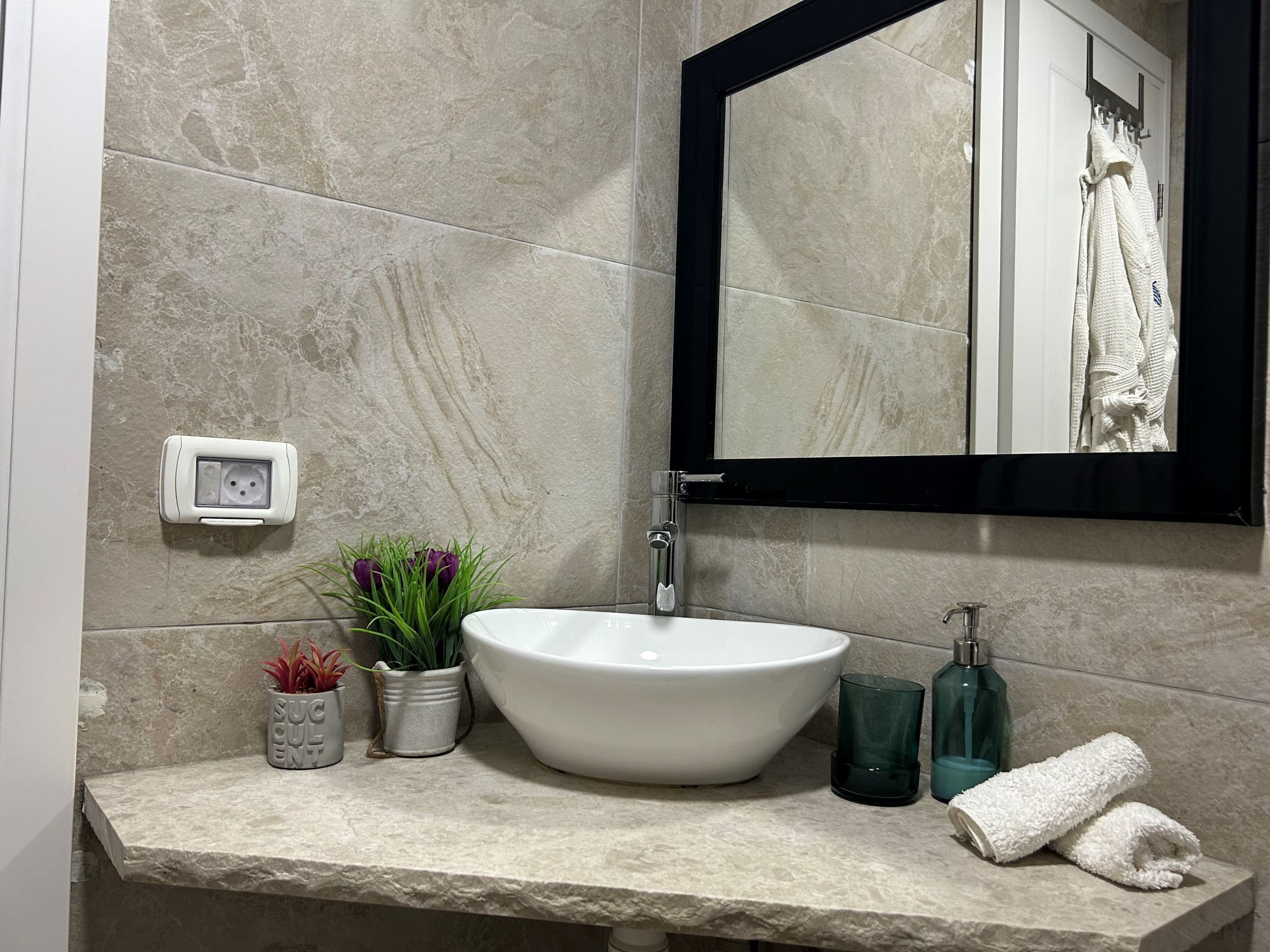 A bathroom with a white sink, a mirror, a towel, and two potted plants.