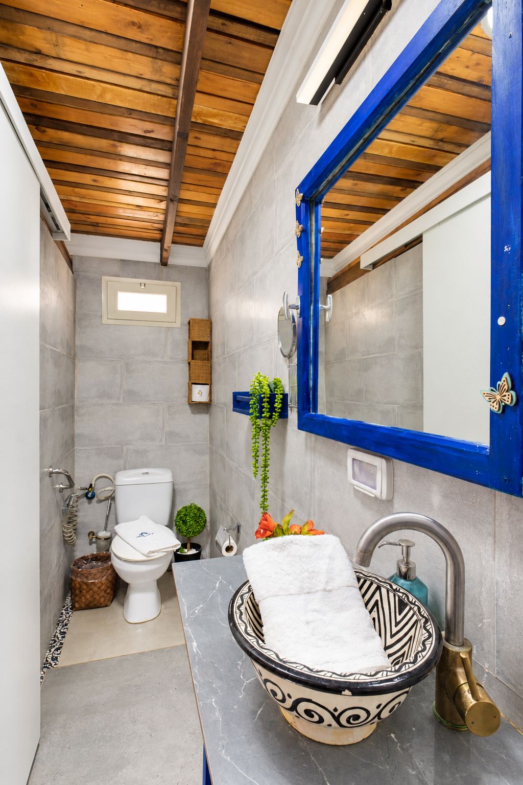 A bathroom with a white toilet, a sink with a decorative bowl, a blue-framed mirror, and a shower area.