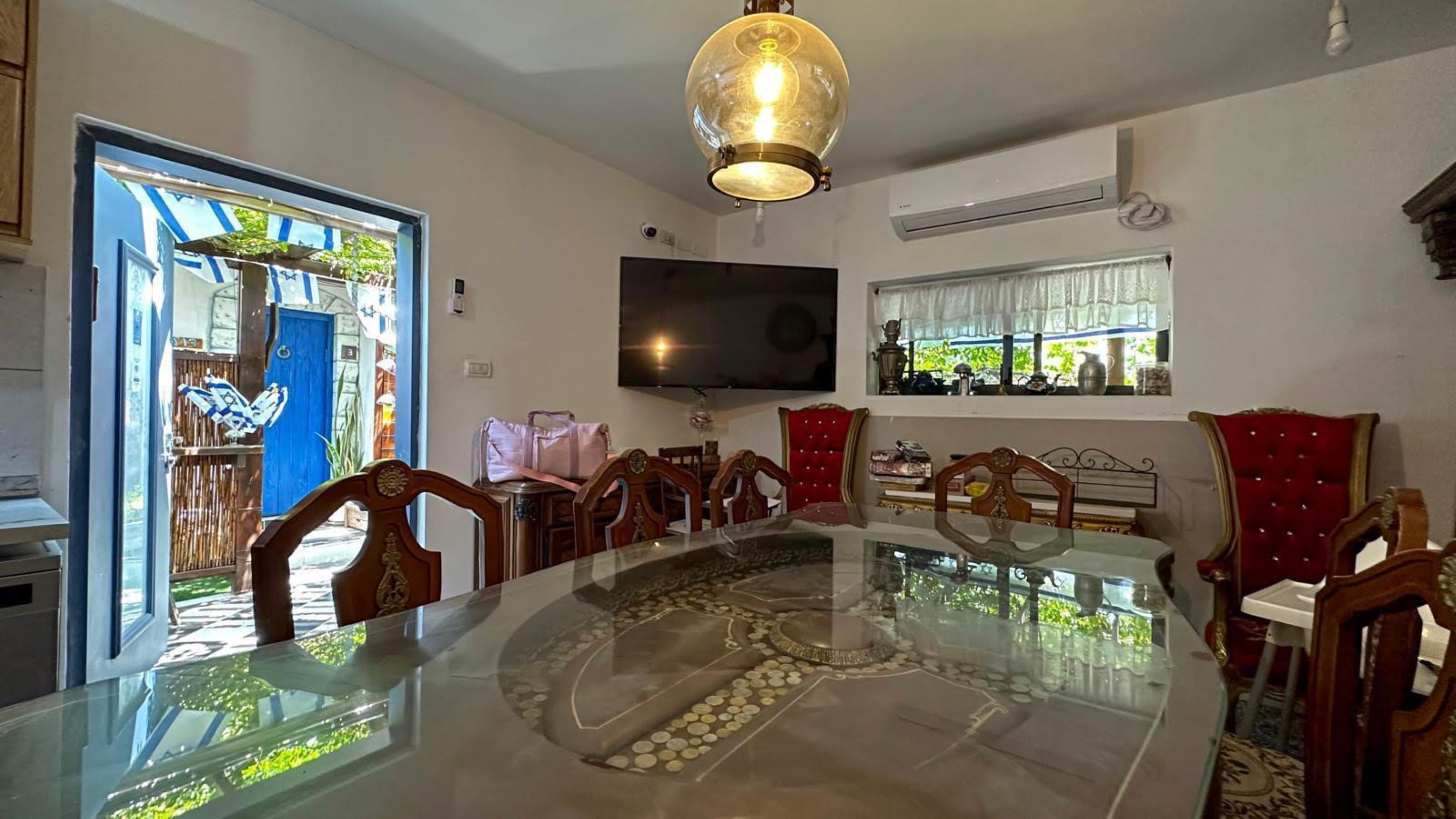 A dining area with a glass table, wooden chairs, and a large TV mounted on the wall.