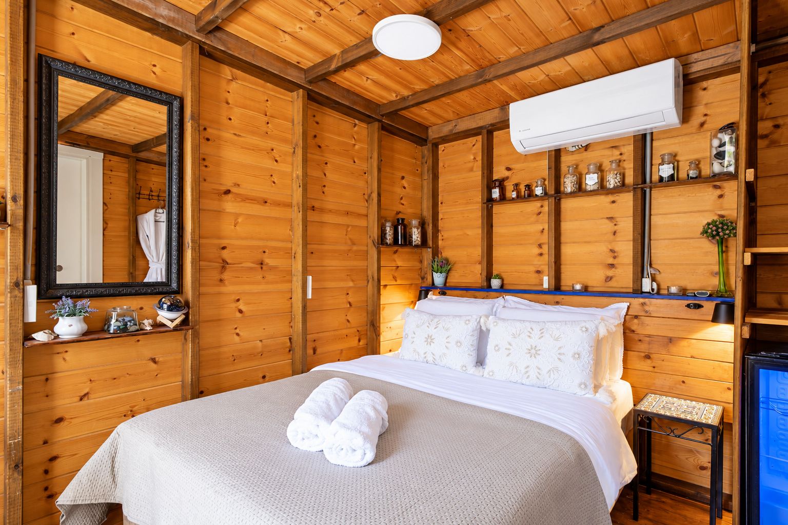 Un dormitorio con paneles de madera, una cama, un espejo, estanterías con adornos y un equipo de aire acondicionado.
