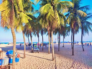 A beach with palm trees, a sandy shore, and beach chairs. -  Hostel Princess Copacabana (Rio de Janeiro)
