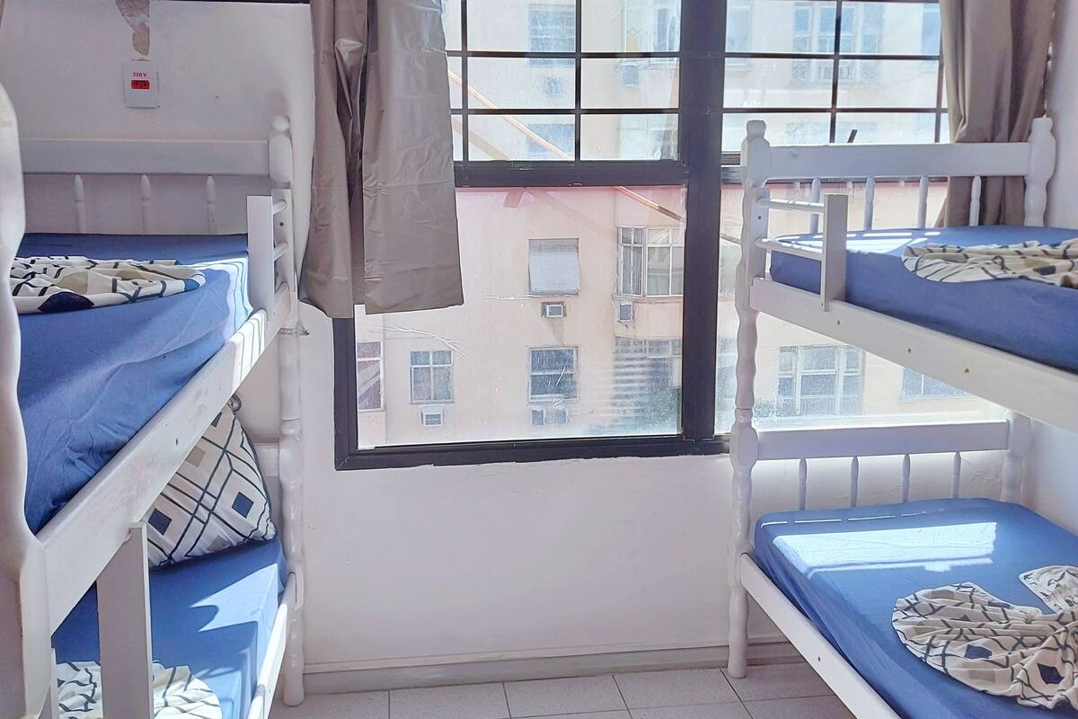 A dormitory room with bunk beds, a window with curtains, and a wall-mounted air conditioning unit.