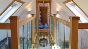 Una escalera con barandillas de madera y paneles de vidrio que conduce a un rellano con una puerta y una pequeña mesa.