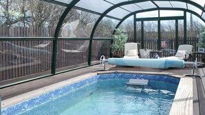 A swimming pool with a glass enclosure, wooden deck, and lounge chairs.