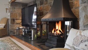 A stone fireplace with a modern stove, a television, and a cozy seating area with a rug.