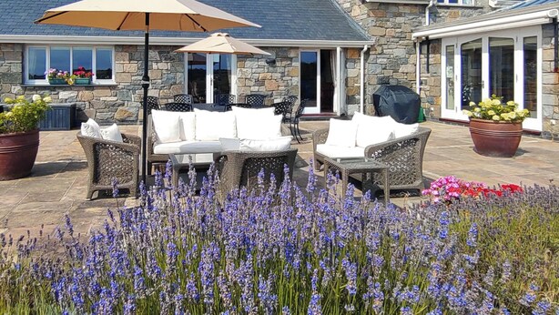 A stone building with a patio area featuring outdoor furniture and a flower garden.